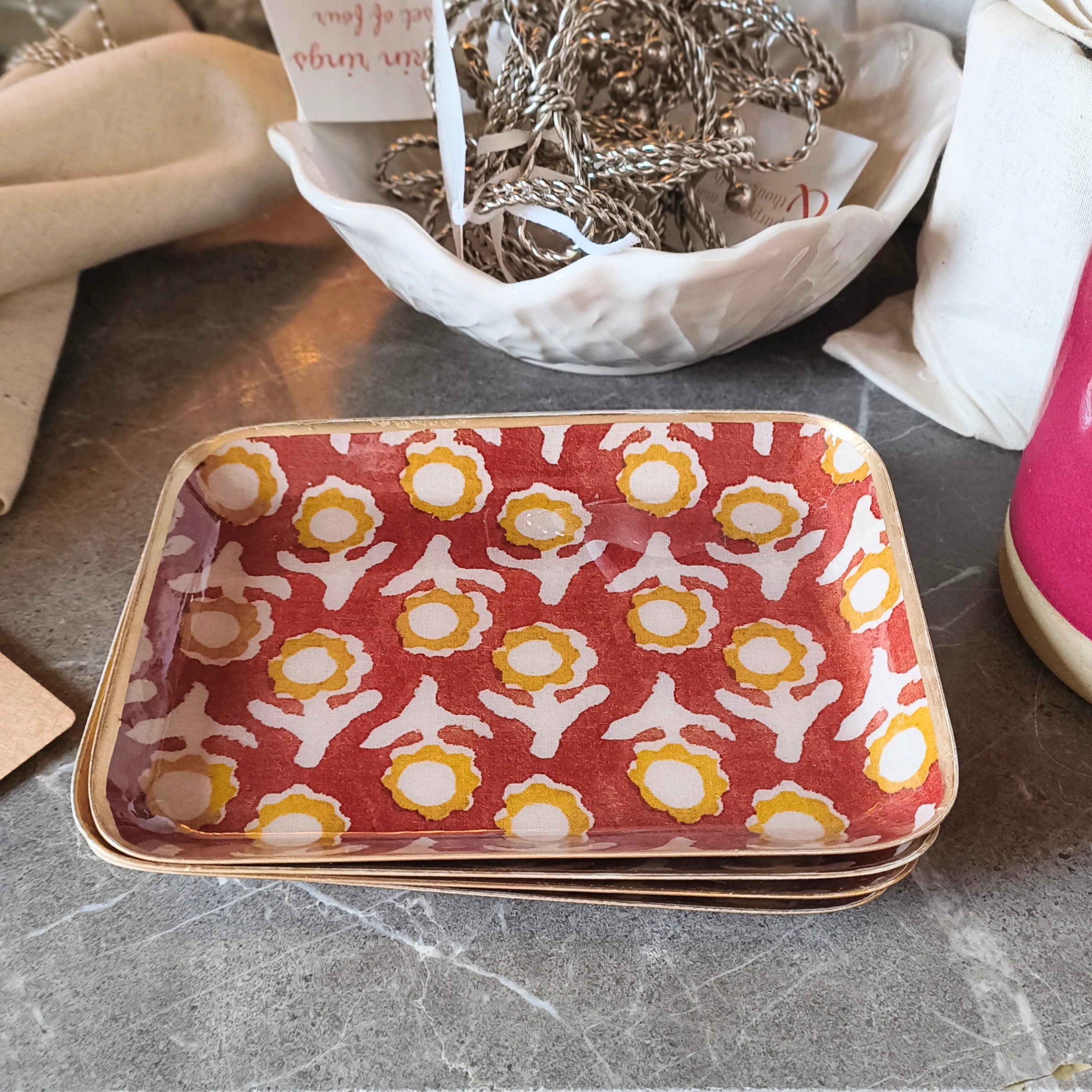 Stack of patterned ceramic trays on a marble surface with various items in the background.