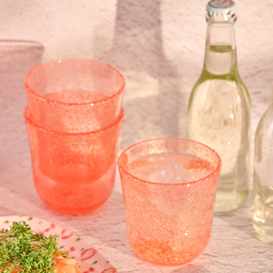 Pink glass tumblers, a plate with food, and bottles on a textured surface.