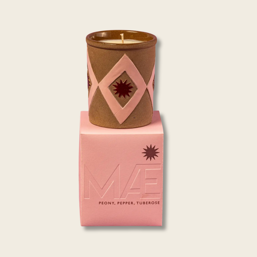 Candle in a decorative brown container on a pink box with branding