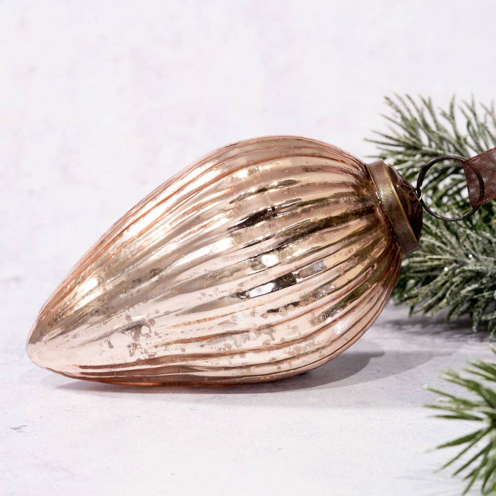 Decorative glass ornament shaped like an almond with ribbed texture, on a light background with greenery.