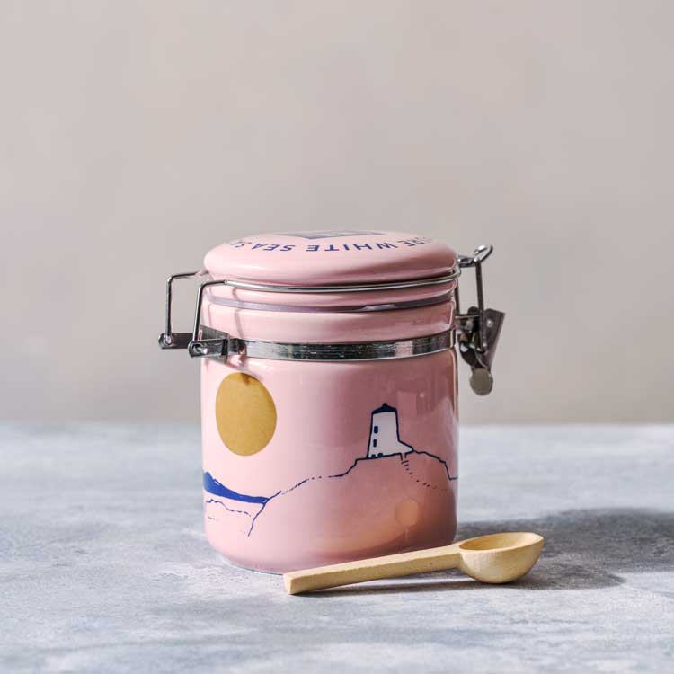 Pink jar with a lid and a wooden spoon on a light surface