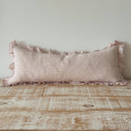 Striped pillow with tassels on a wooden surface against a light gray wall