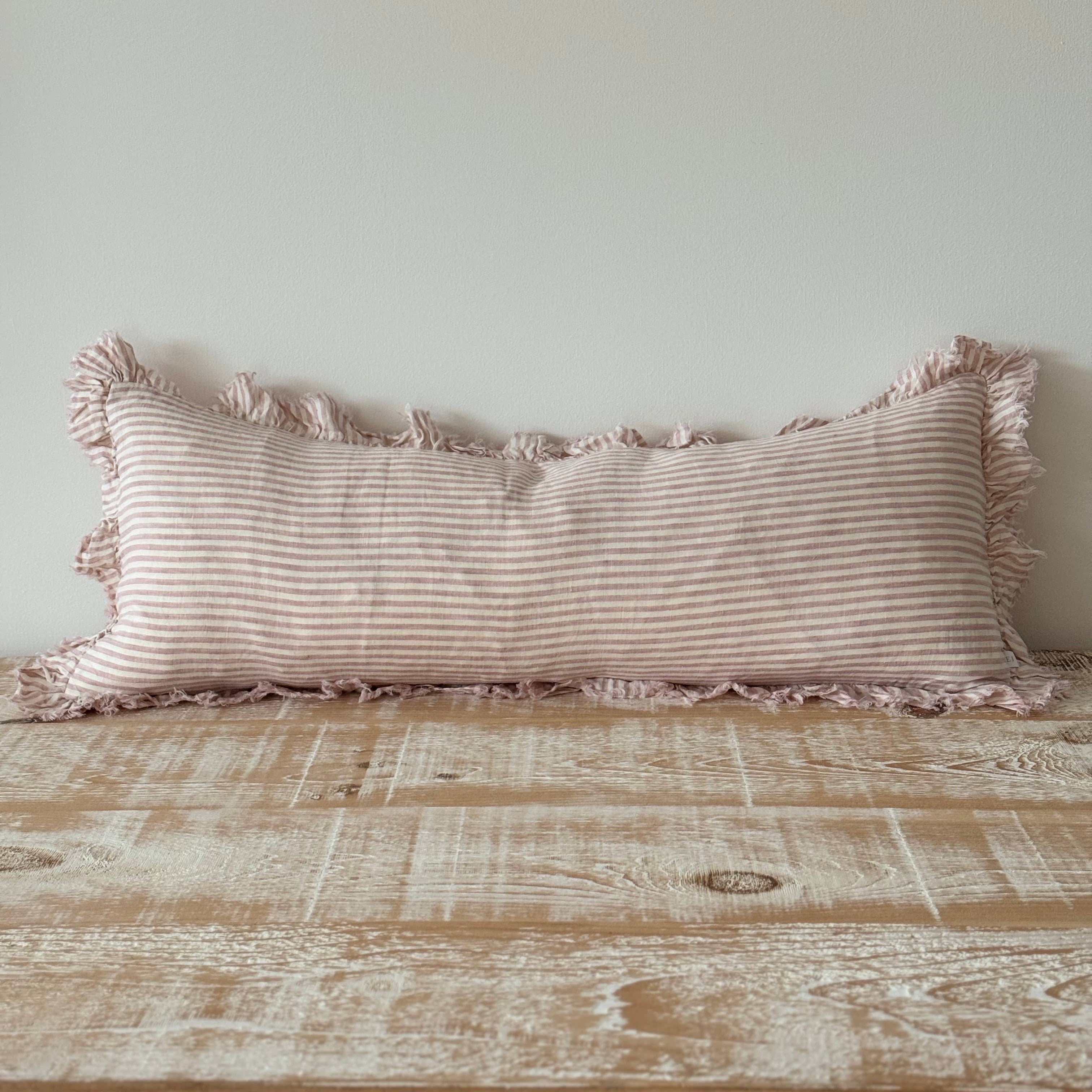 Striped pillow with tassels on a wooden surface against a light gray wall