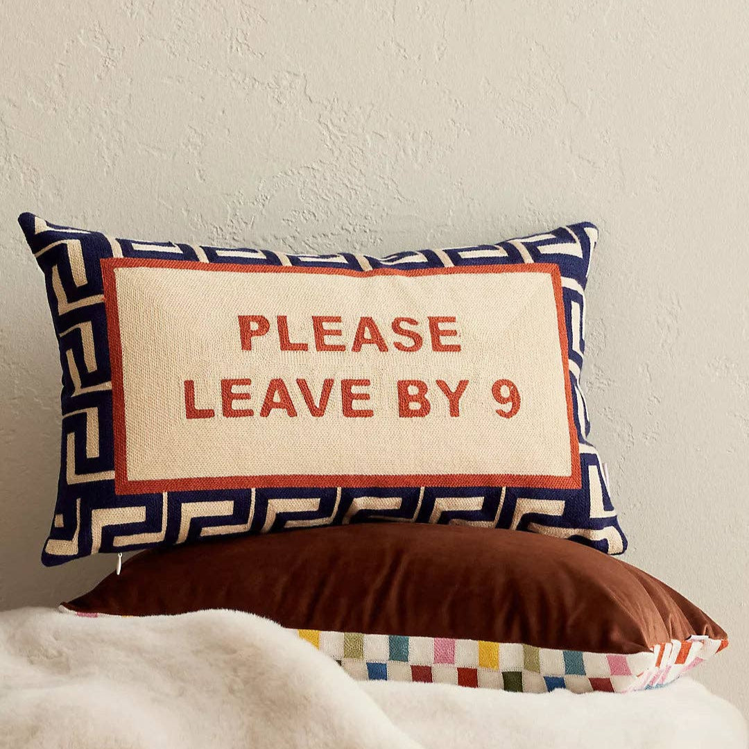 Decorative pillow with 'Please Leave By 9' text on a plain background
