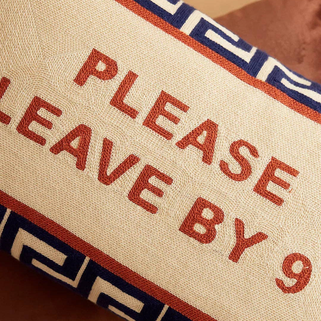 Cushion with 'Please Leave by 9' text on a wooden floor
