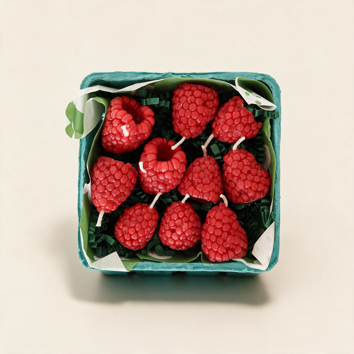 Set of ten raspberry-shaped beeswax candles in a berry basket on a cream background