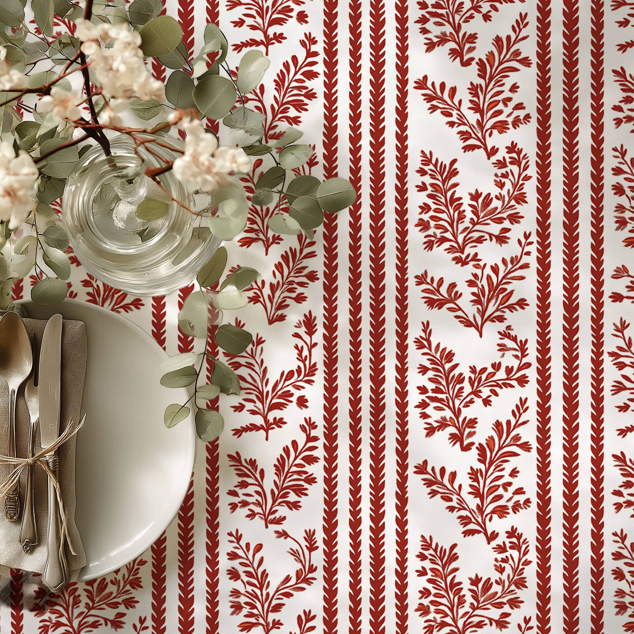 Table setting with red and white patterned tablecloth, white plates, and silverware.
