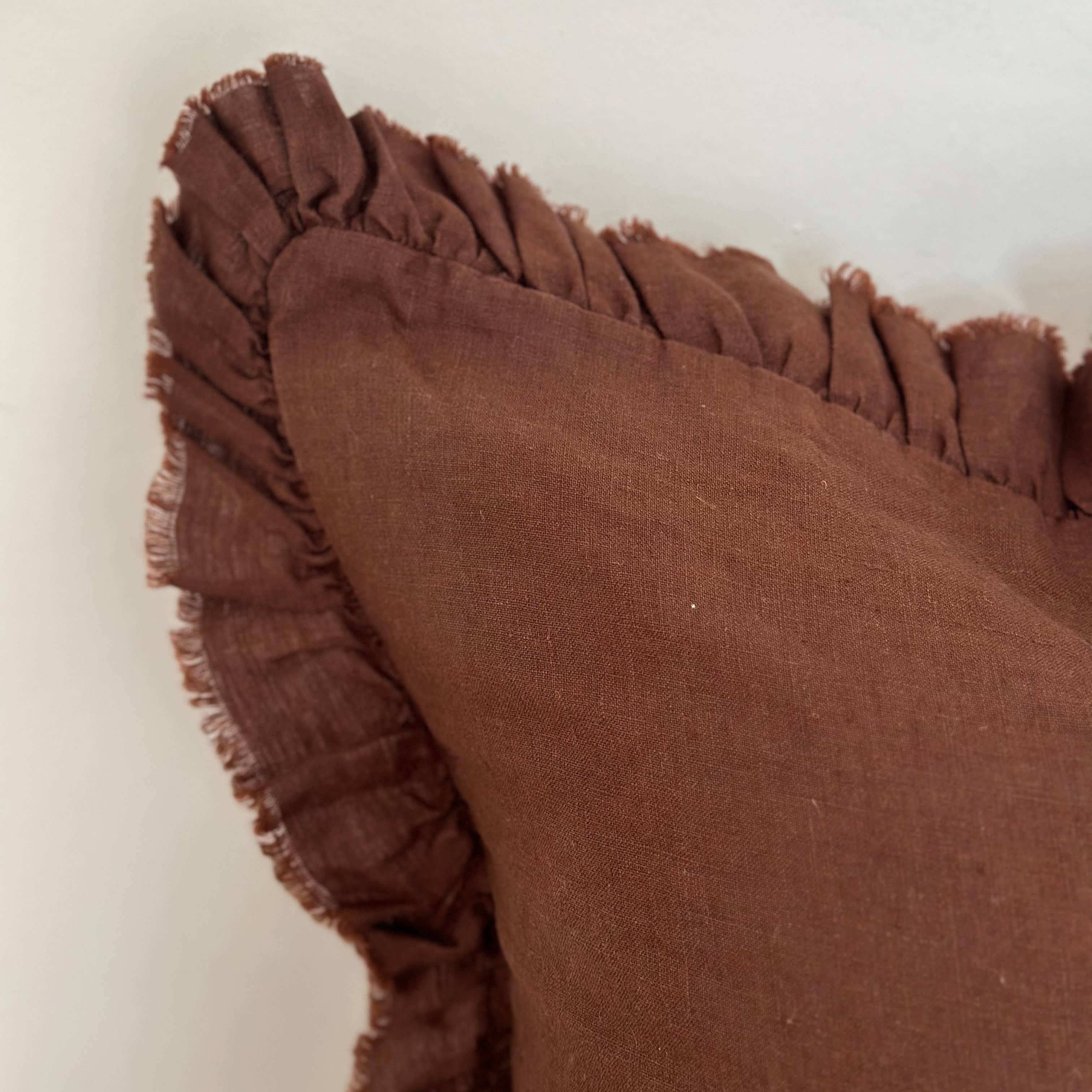 Brown pillow with ruffled edge on a light beige background
