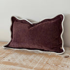 Plum pillow with white trim on a wooden surface against a light gray wall