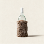Tan sheepskin wine cooler holding a bottle of wine, on a cream background