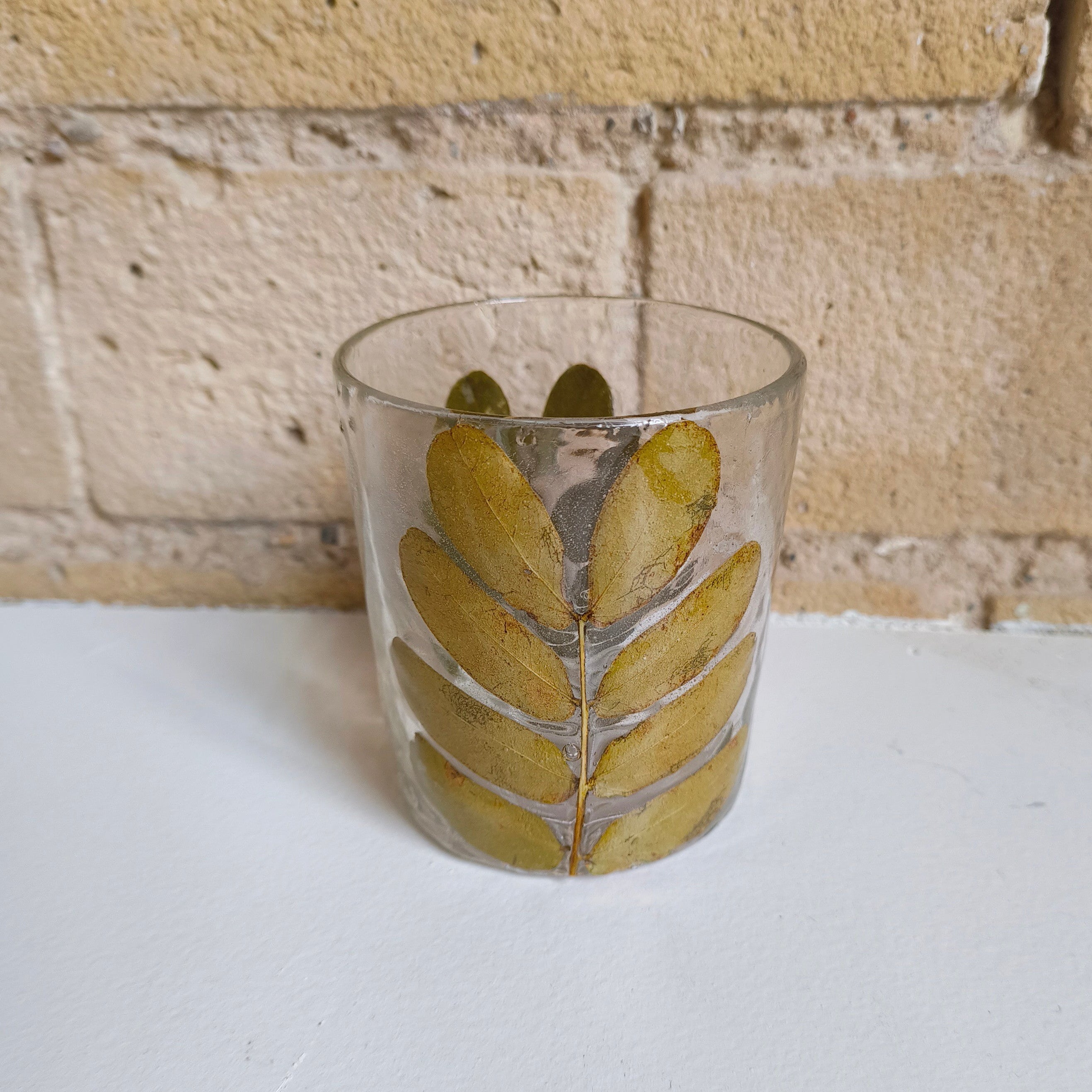 Clear glass with leaf design on a white surface and stone wall background