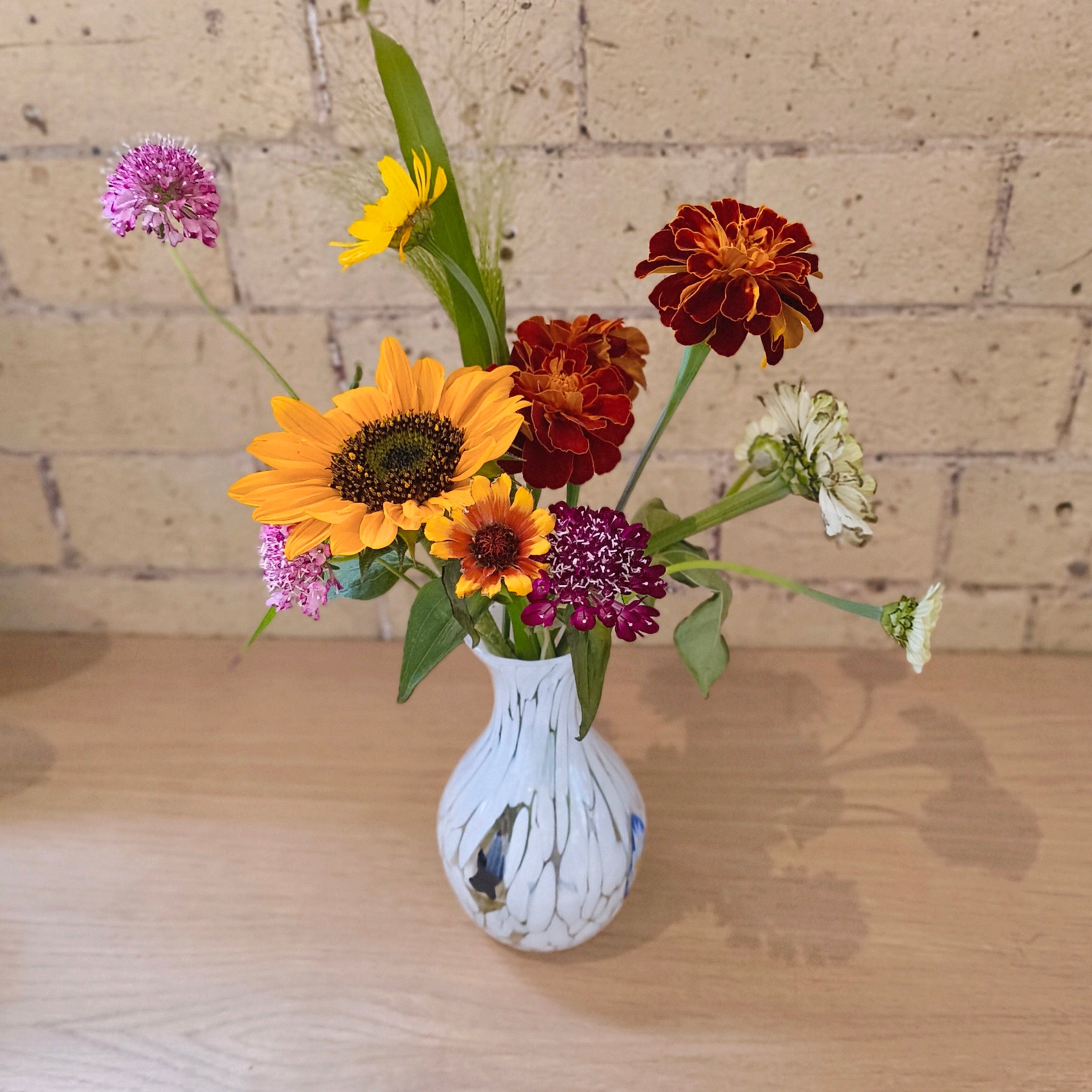 Vase with colorful flowers on a wooden surface against a brick wall background
