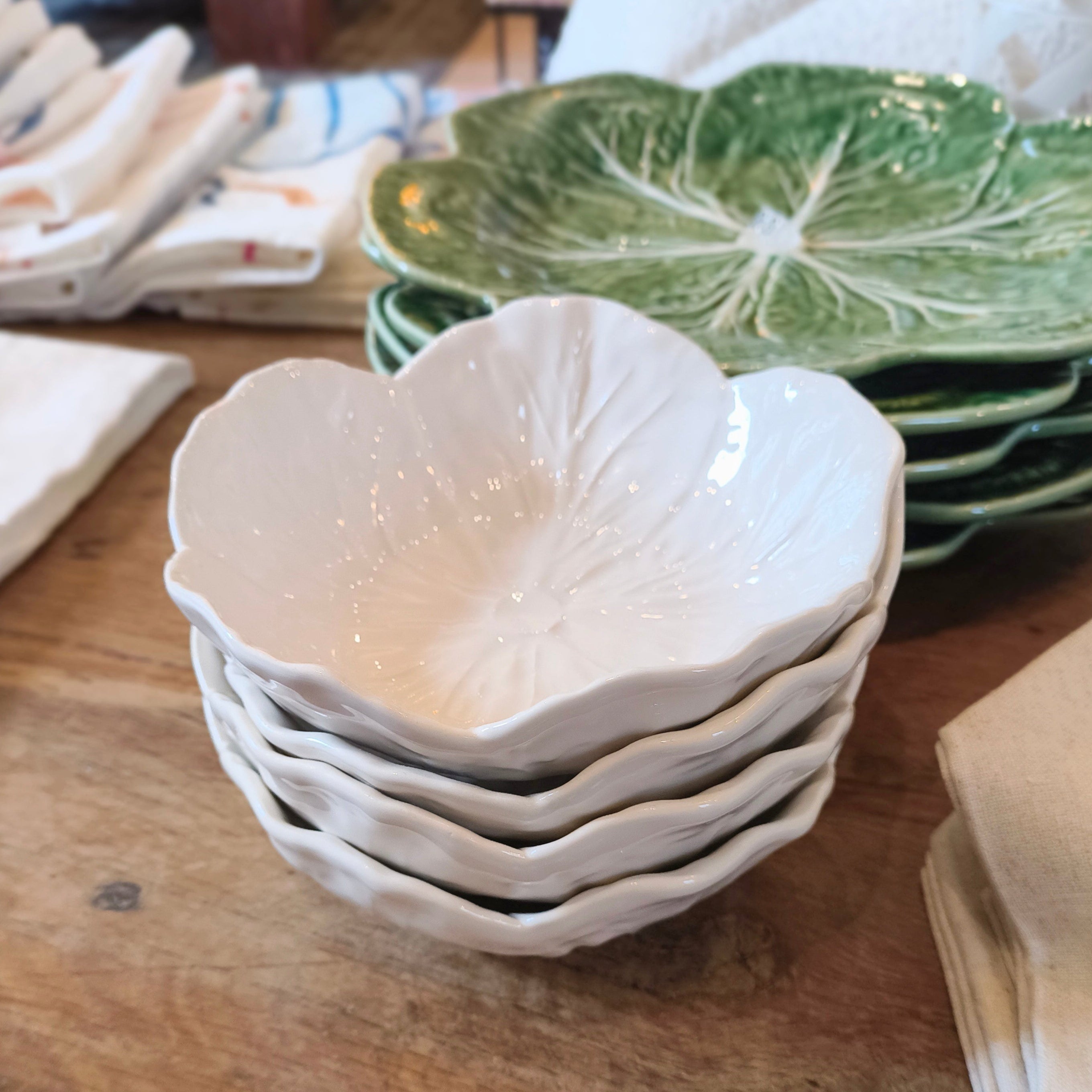 Stack of white ceramic bowls on a wooden table with green leaf-patterned plates in the background.