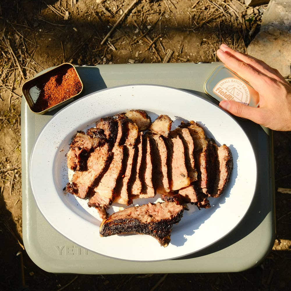 Grilled meat on a plate with a side of spices on a camping stove
