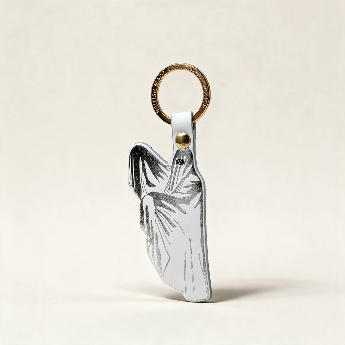 Spoo-key ghost key fob in white foil-embossed leather with a gold-plated ring, on a cream background
