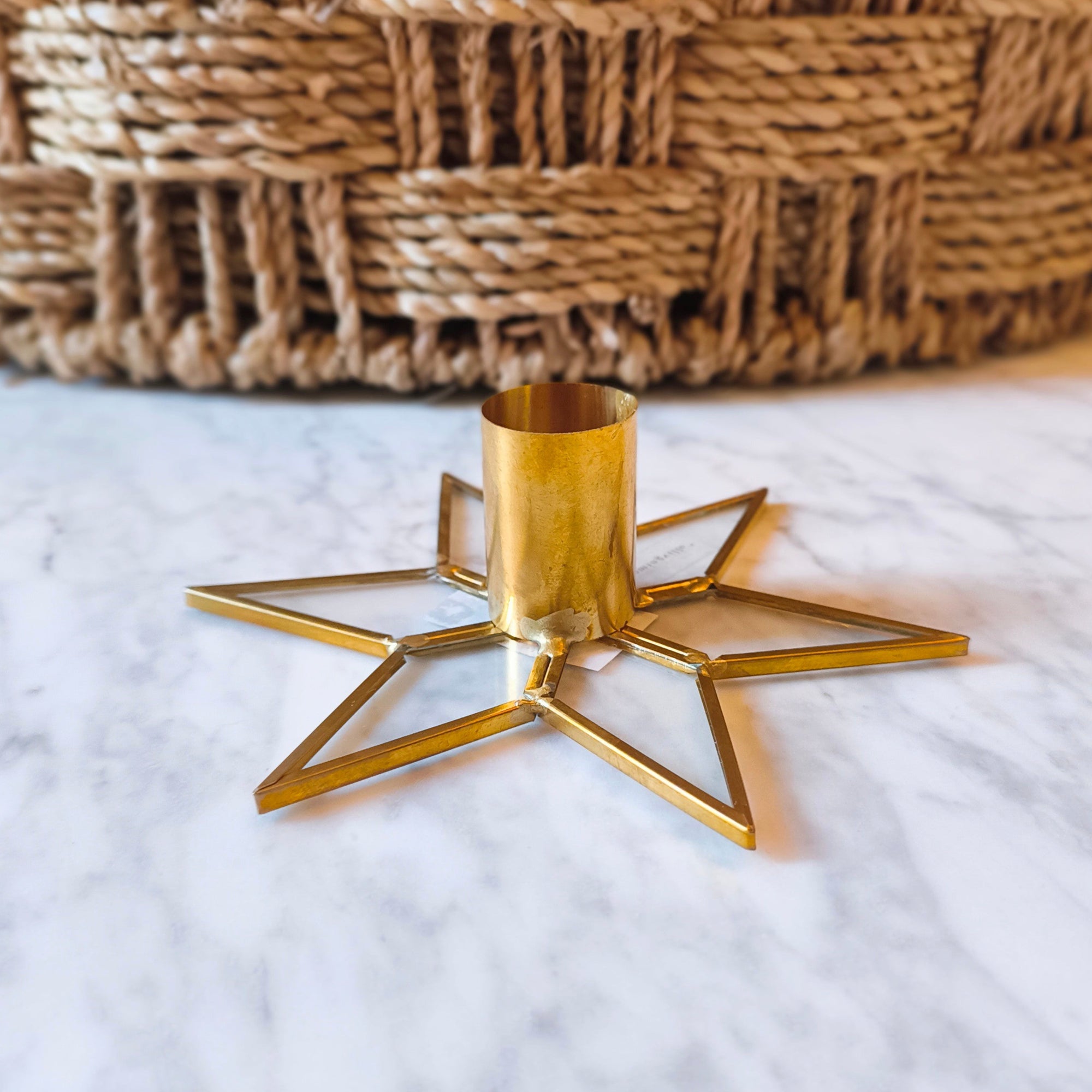 Gold star-shaped candle holder on a marble surface with a woven basket in the background.