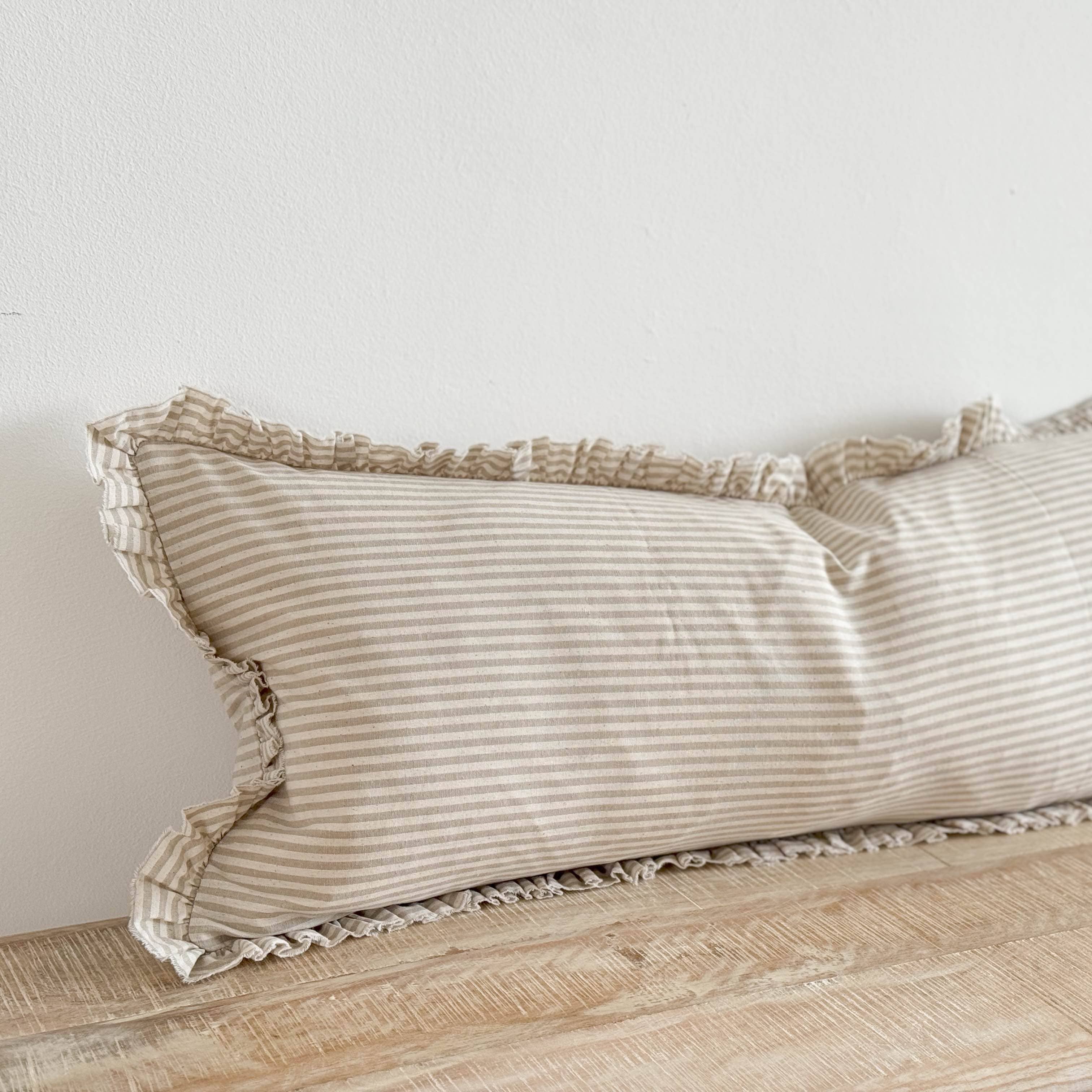 Striped pillow with ruffled edges on a wooden surface against a white wall