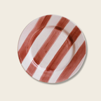 Round ceramic plate with red and white striped pattern on a beige background