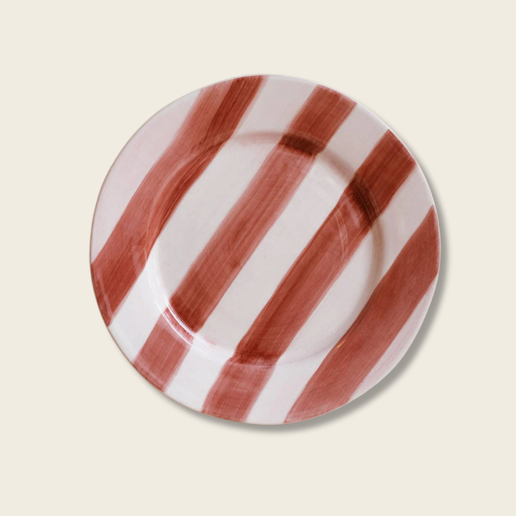 Round ceramic plate with red and white striped pattern on a beige background