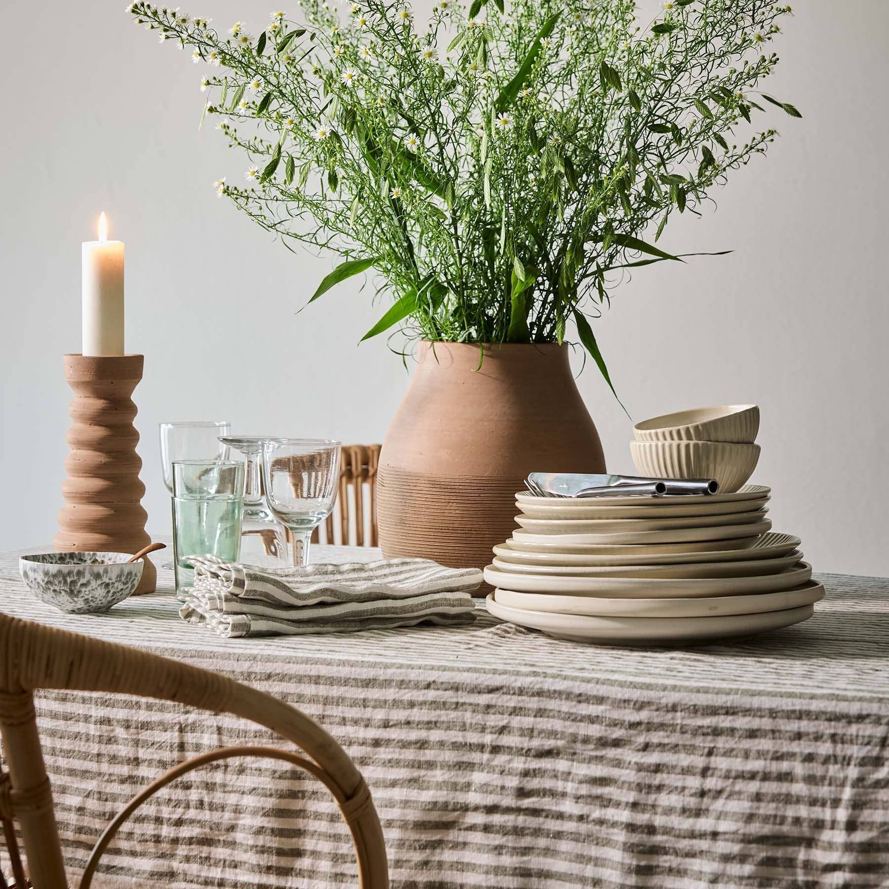 Table setting with a vase of greenery, candles, and ceramic items on a neutral background