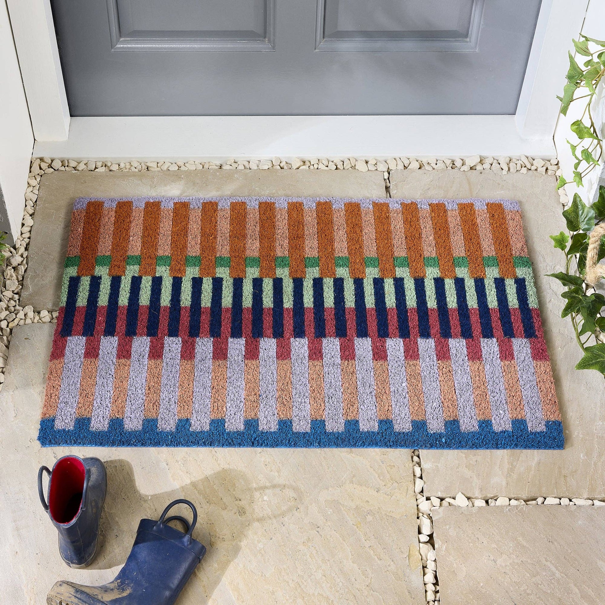 Colorful striped doormat on a stone patio with a gray door in the background.