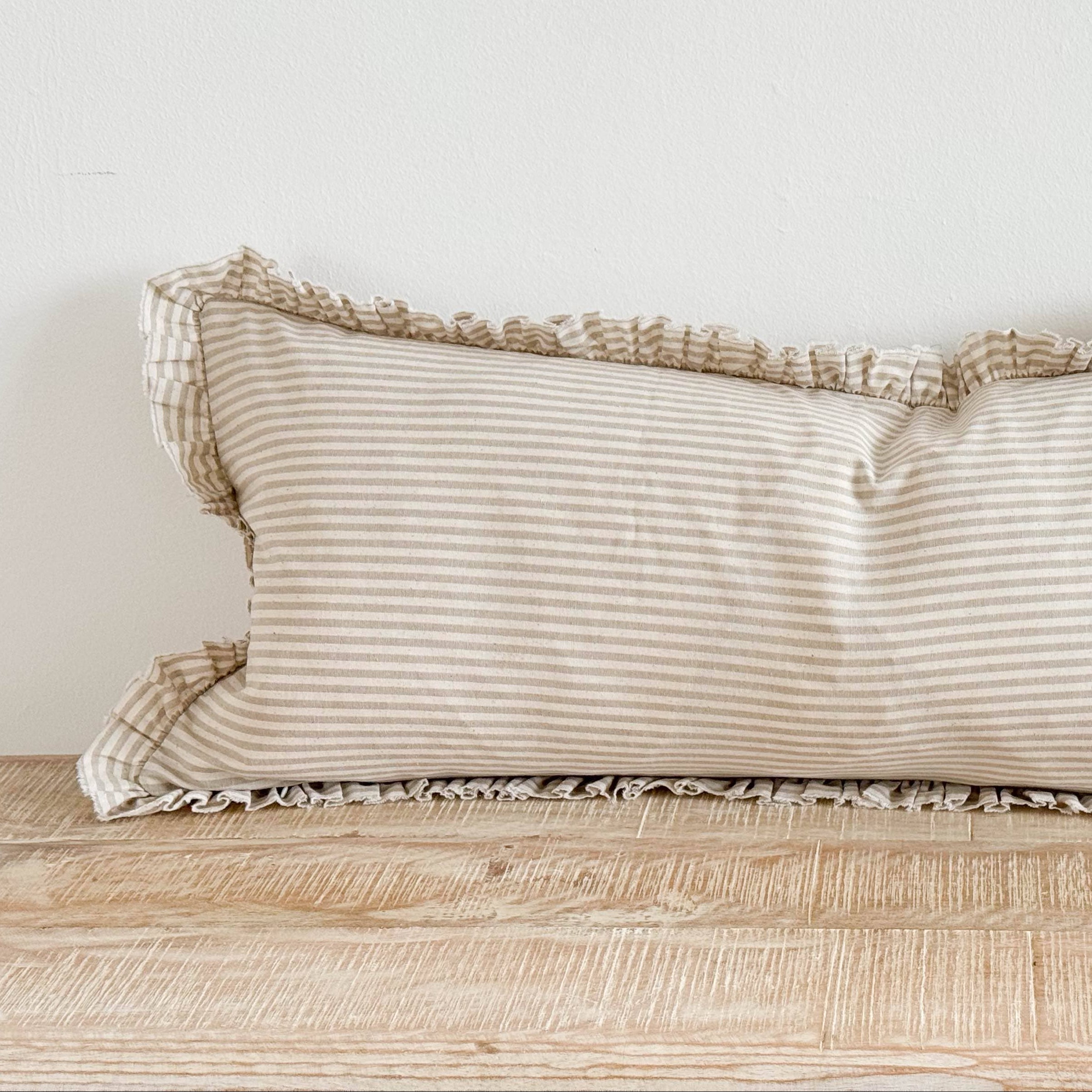 Beige striped pillow with ruffled edges on a wooden surface