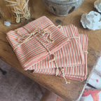 Stack of orange and white striped fabric napkin bundles tied with twine on a wooden surface.