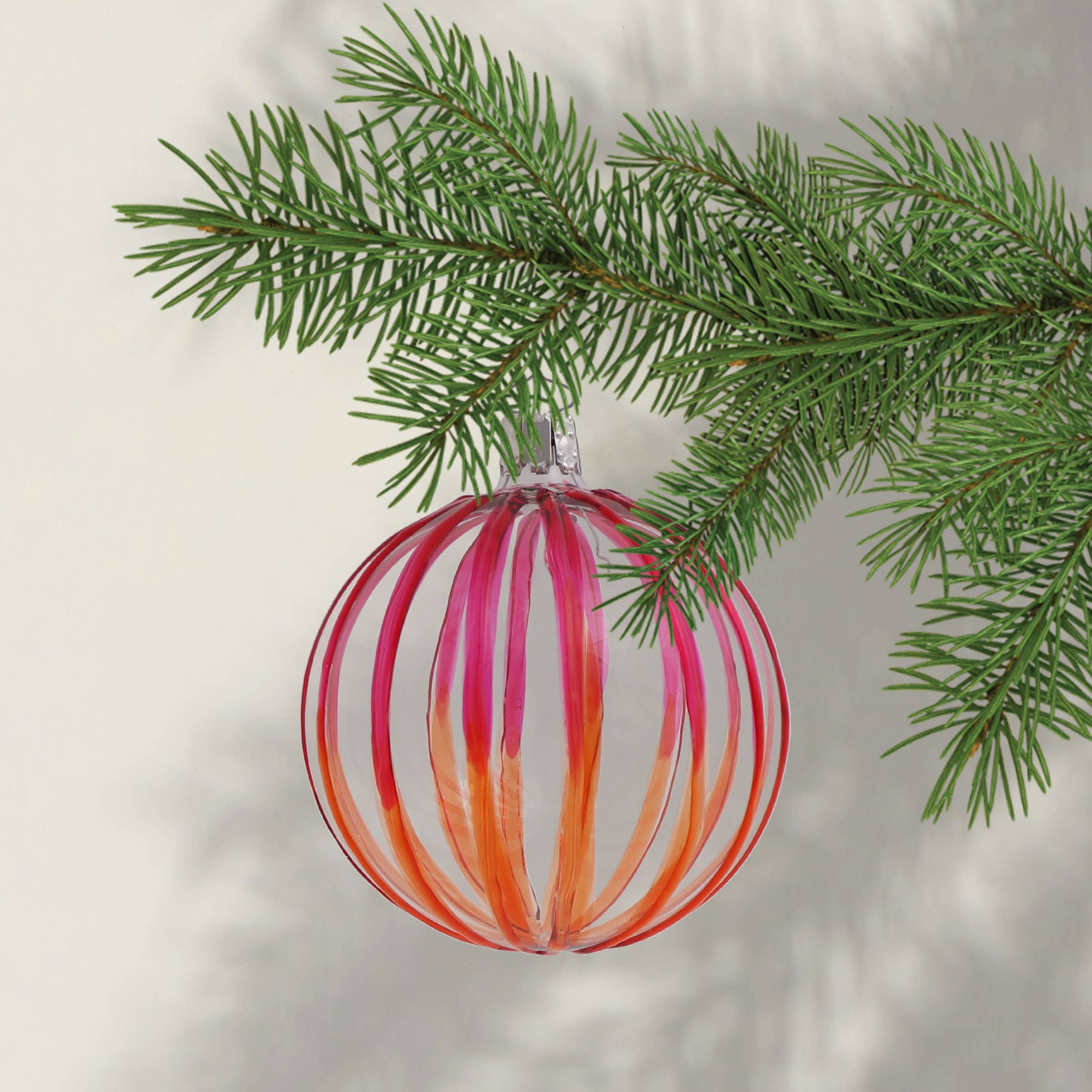 A red and orange striped glass Christmas bauble decoration hanging from a Christmas tree branch.