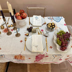 Decorative table setting with fruits, candles, and a patterned tablecloth.