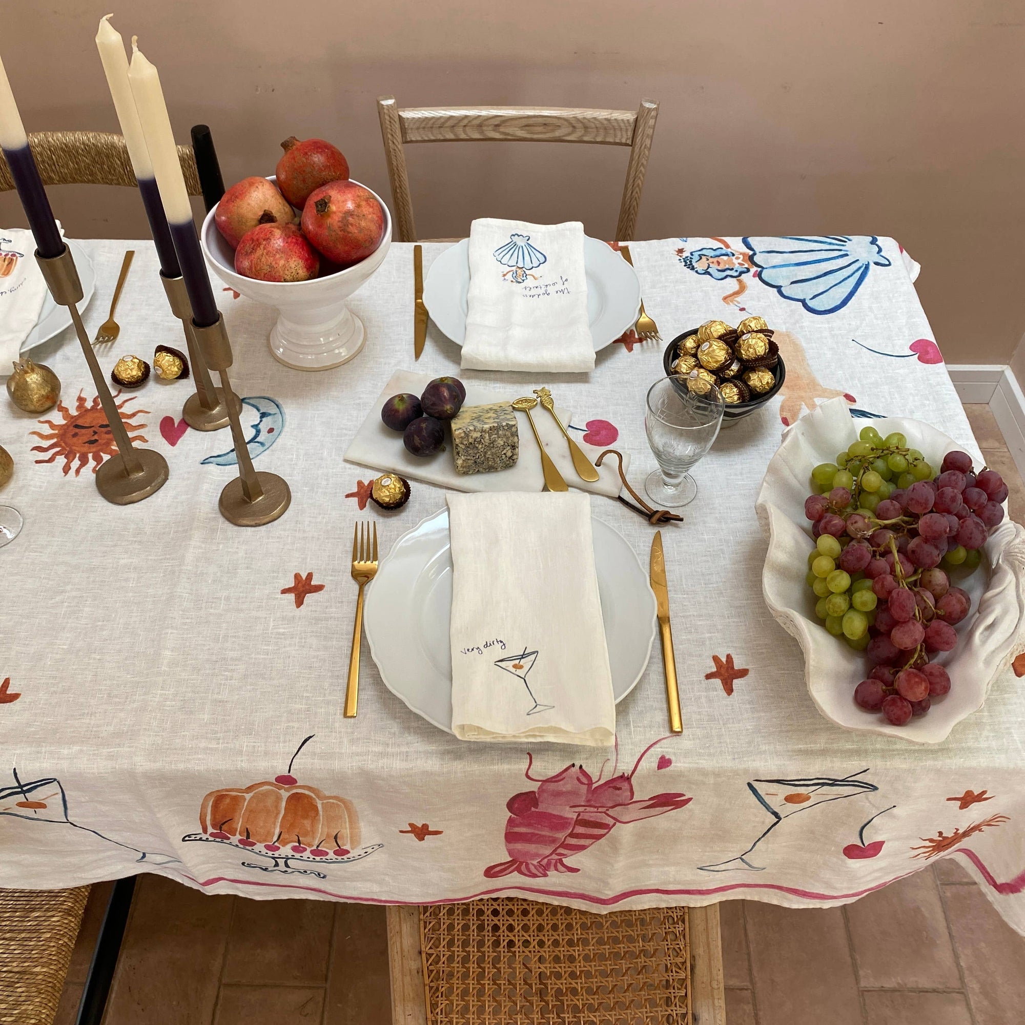 Decorative table setting with fruits, candles, and a patterned tablecloth.