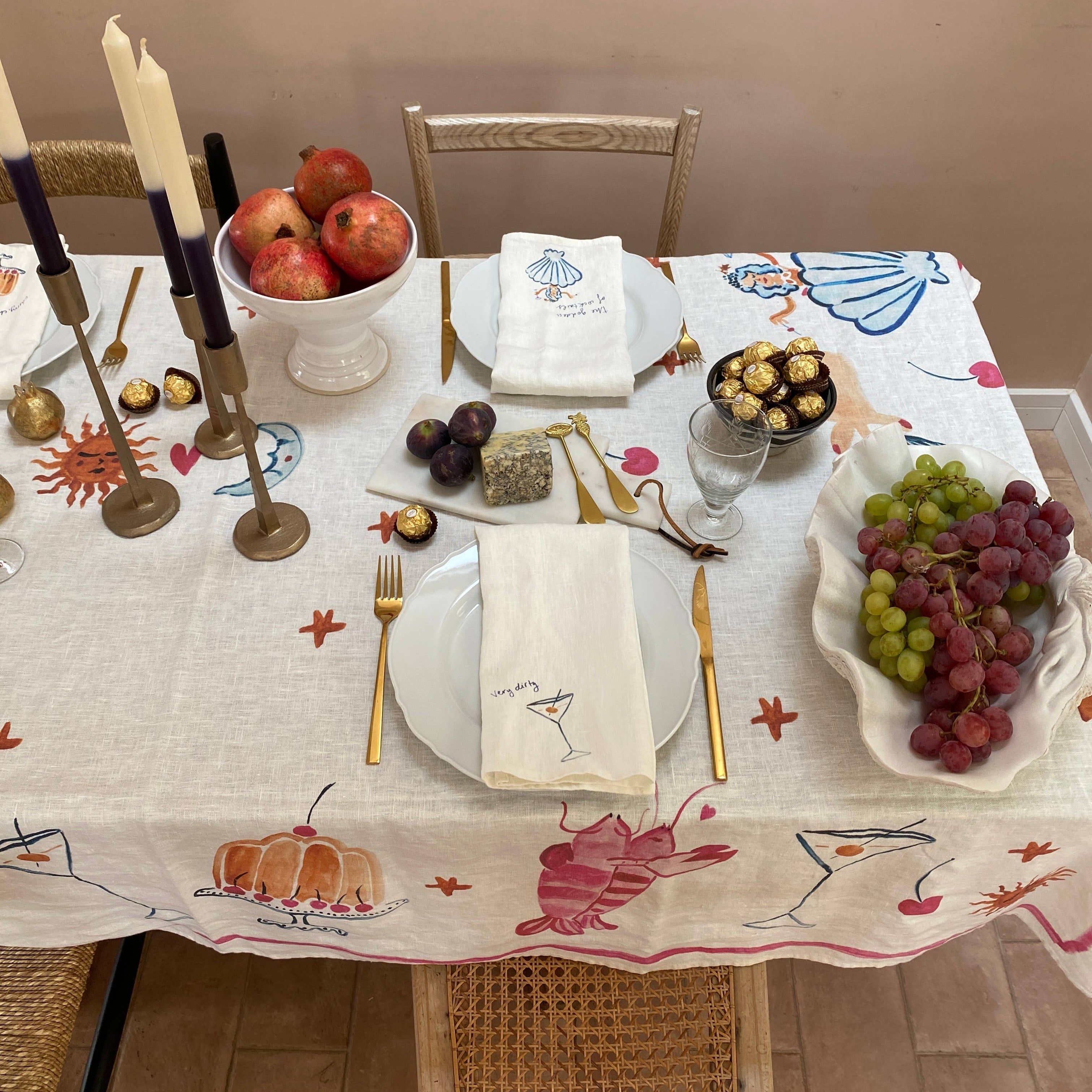 Decorative table setting with fruits, candles, and a patterned tablecloth.