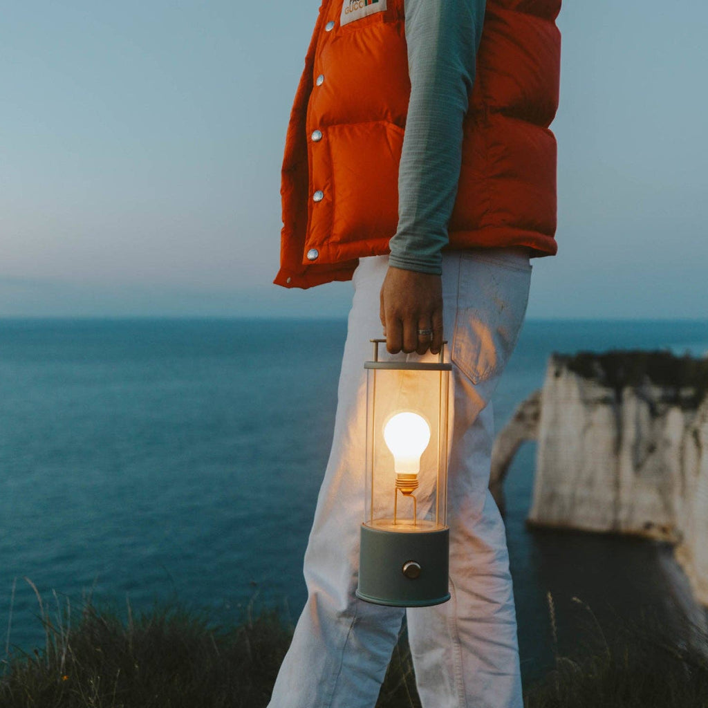 Person holding a lantern by the ocean during sunset