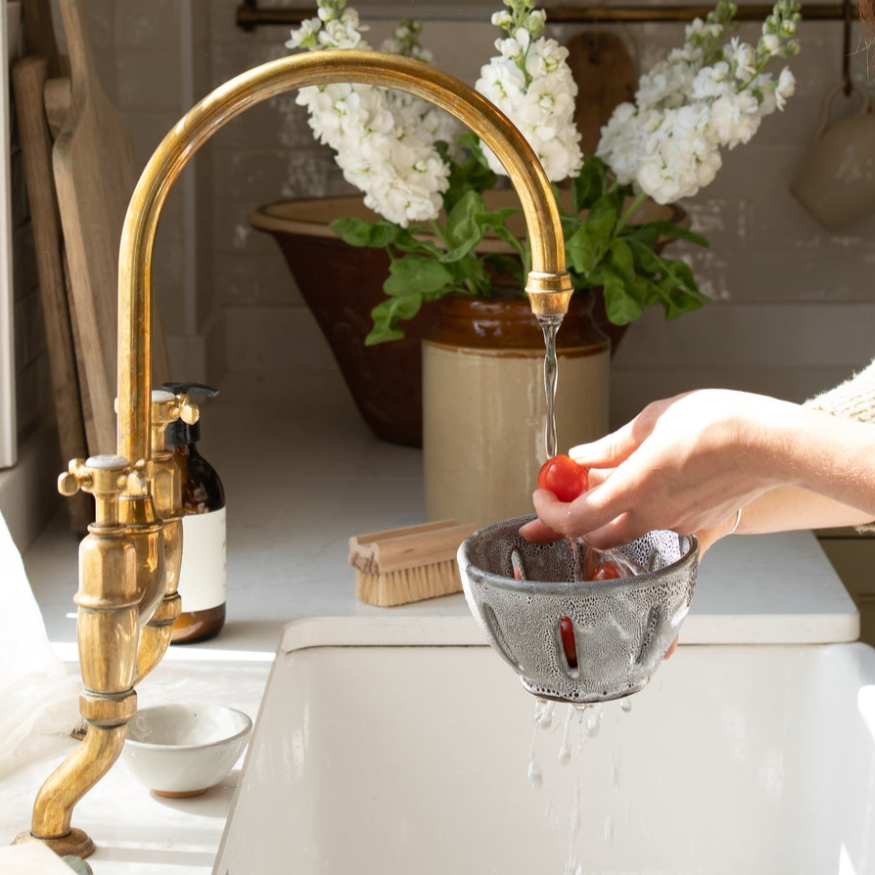 Person washing dishes in a kitchen with a gold faucet and white flowers in the background
