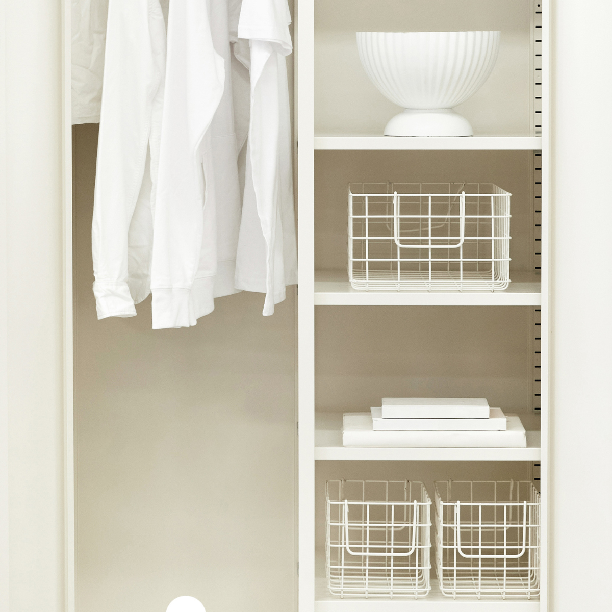 Closet with white shelves and baskets, containing folded clothes and a lamp.