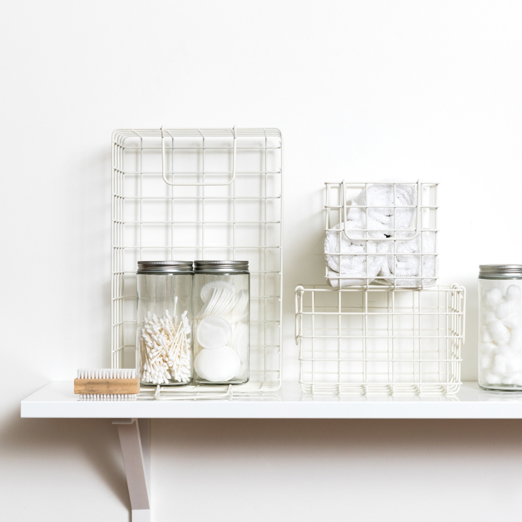 White wire baskets and jars on a white shelf against a white background
