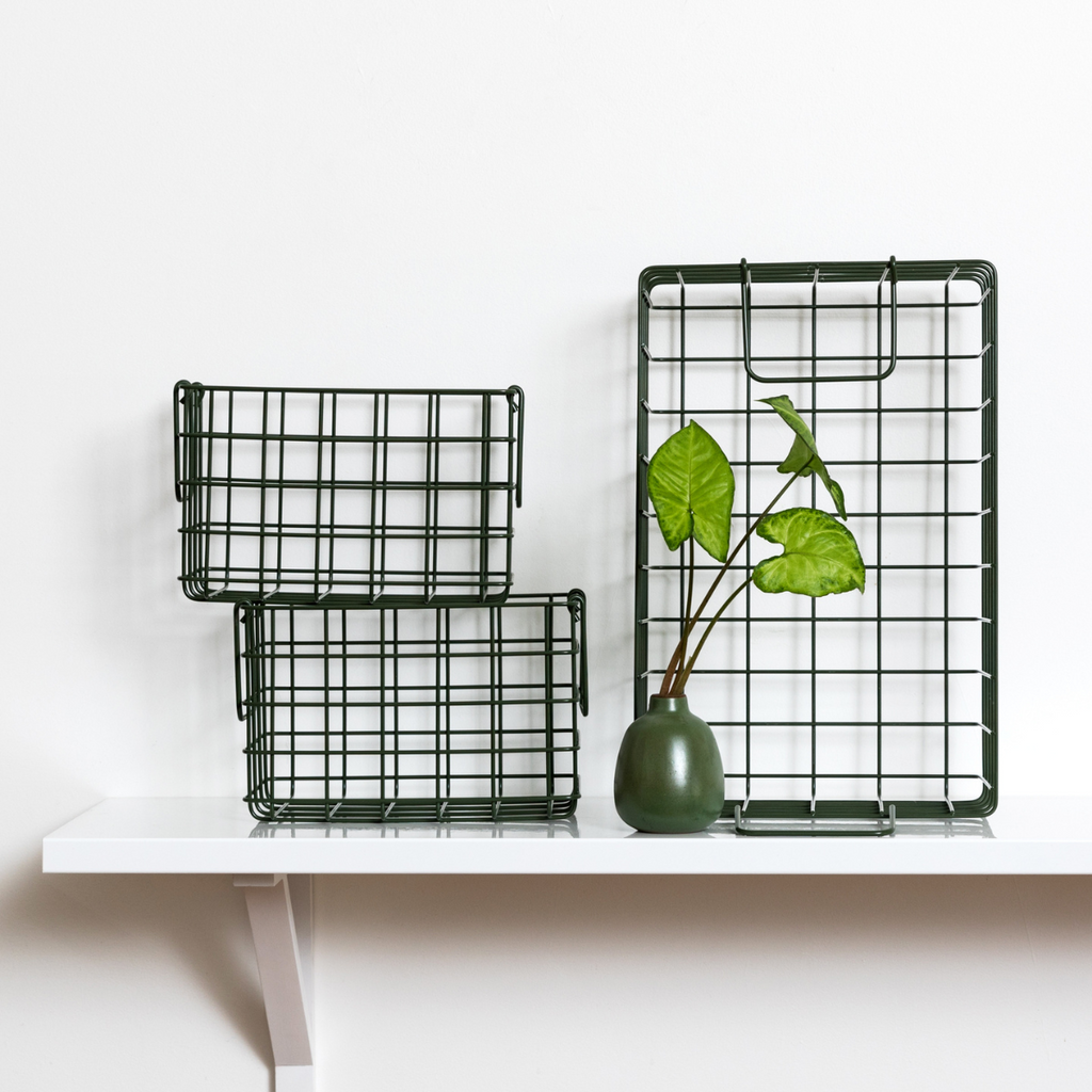 Two black wire baskets on a white shelf with a green vase and leaves.