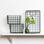 Two black wire baskets on a white shelf with a green vase and leaves.