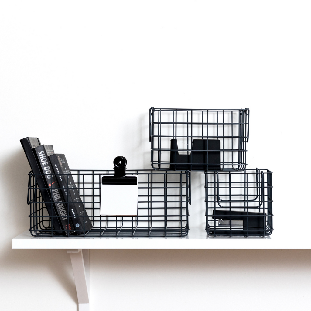 Black wire baskets on a white shelf with books and office supplies.