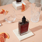 Bottle of red liquid on a table with grapefruit slices and glasses
