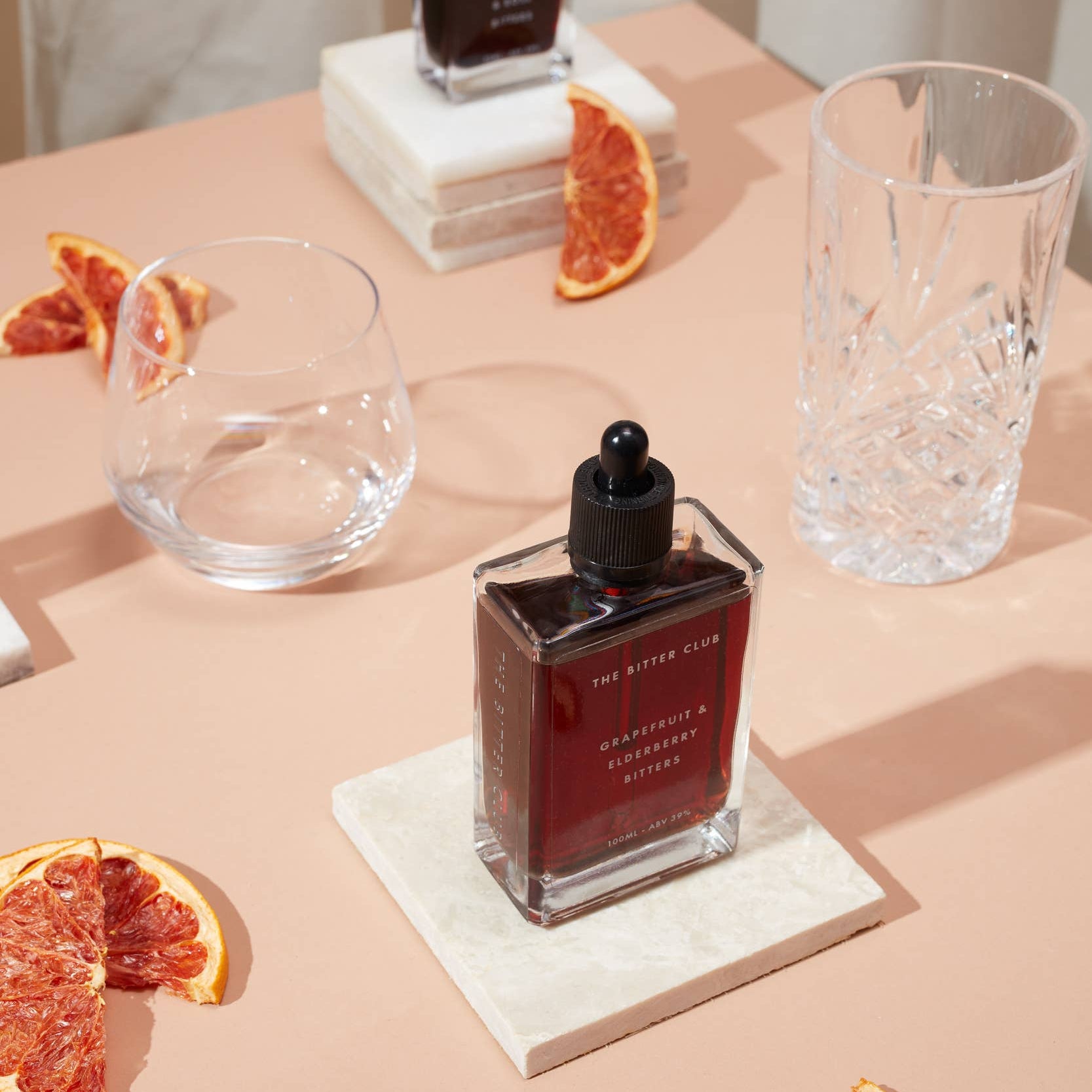 Bottle of red liquid on a table with grapefruit slices and glasses