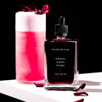 Bitters bottle labeled 'The Bitter Club' next to a pink cocktail with a black background