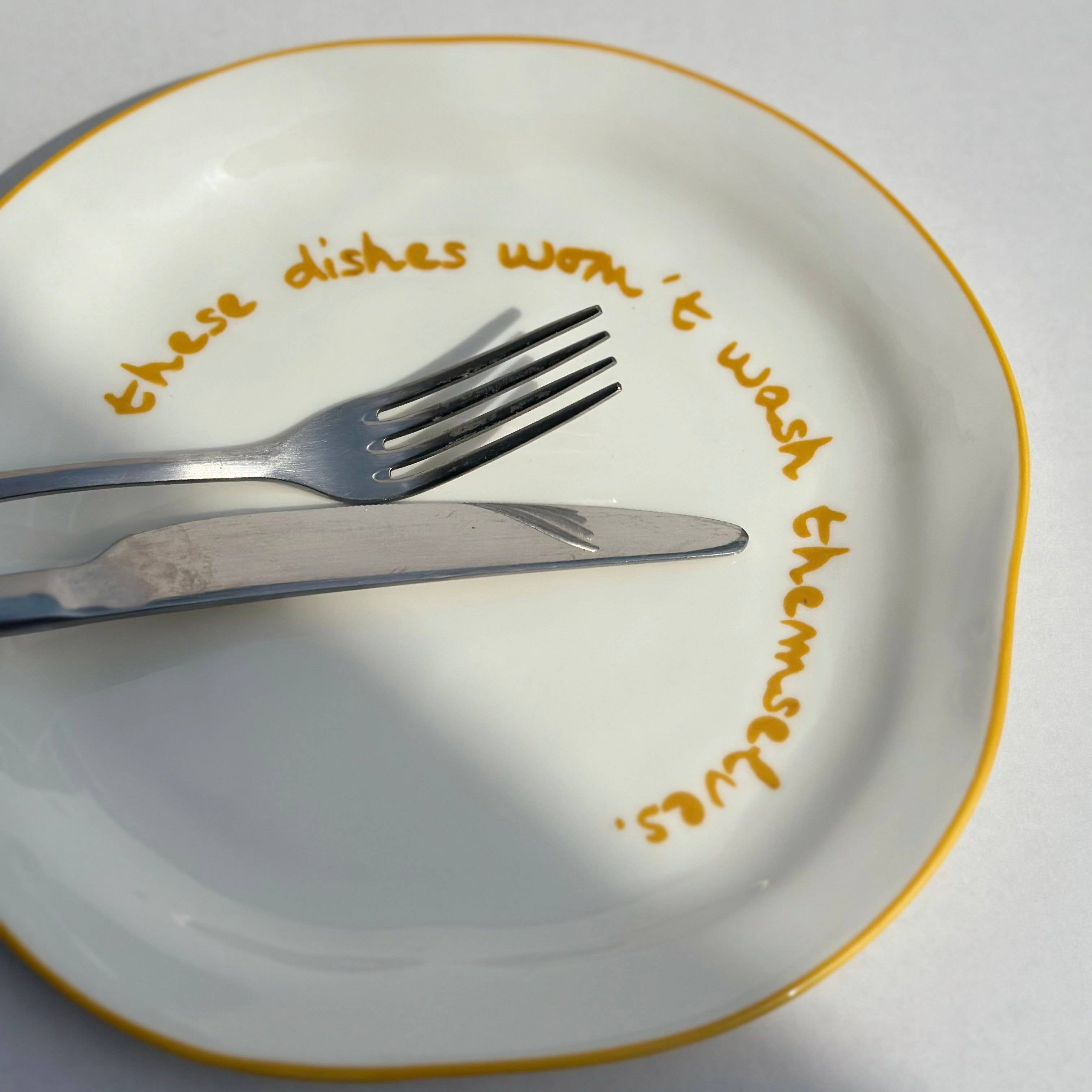 White plate with gold rim, silver fork, and knife, and text 'these dishes were it wash them self' on a white background.