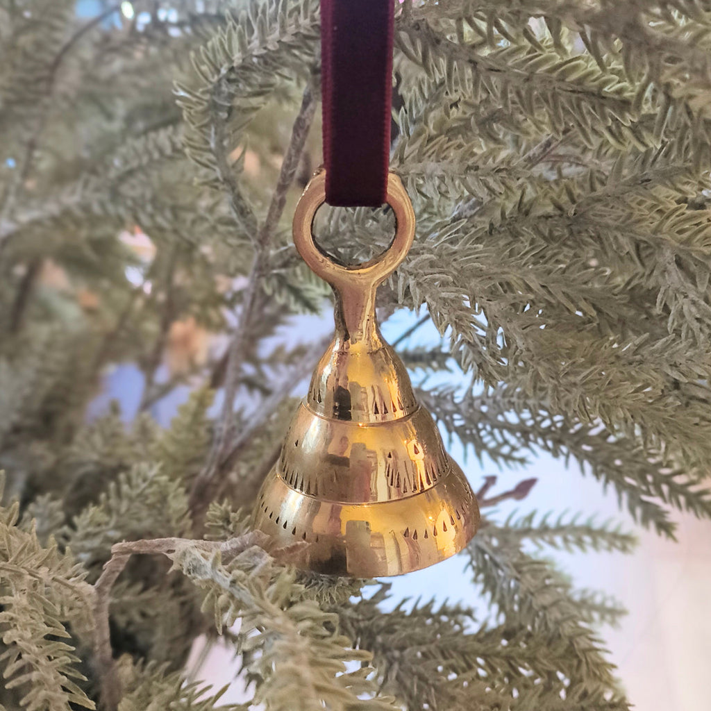 Gold bell ornament hanging on a branch with a blurred background