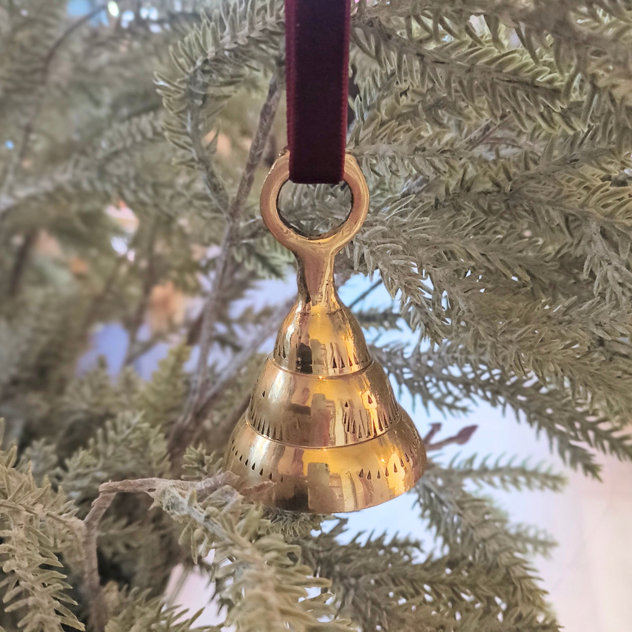 Gold bell ornament hanging on a branch with a blurred background