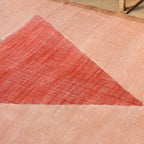 Textured pink rug with a red triangle design on a beige floor.