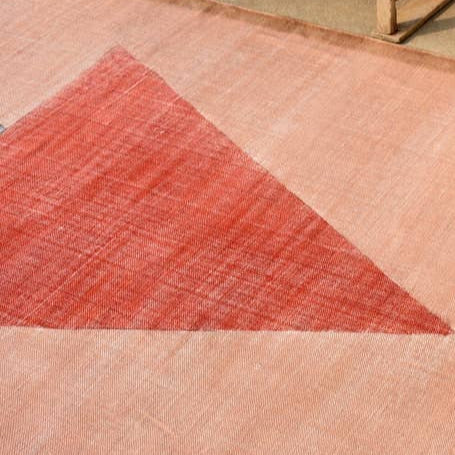 Textured pink rug with a red triangle design on a beige floor.