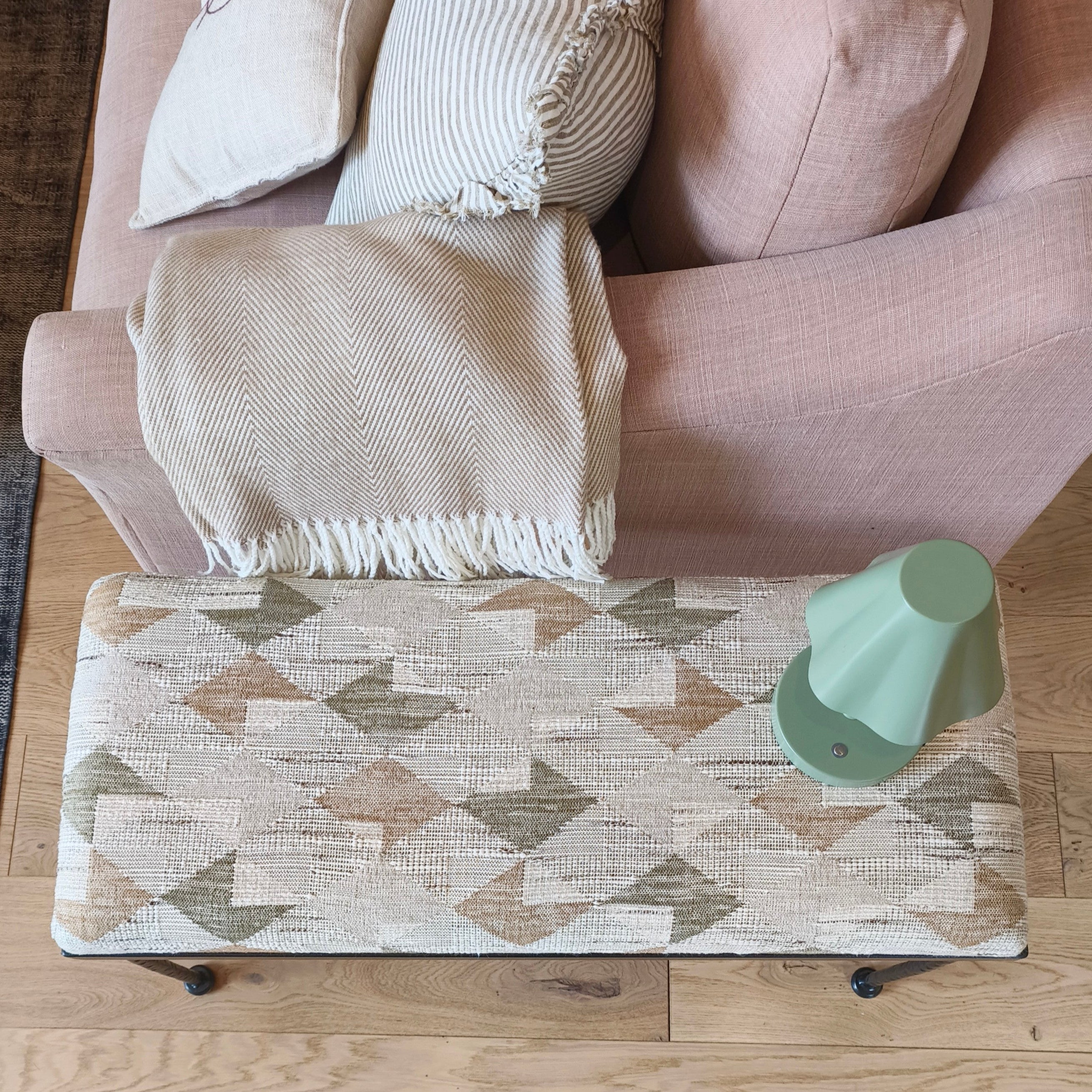 Patterned coffee table in front of a beige sofa with a green cup on it.