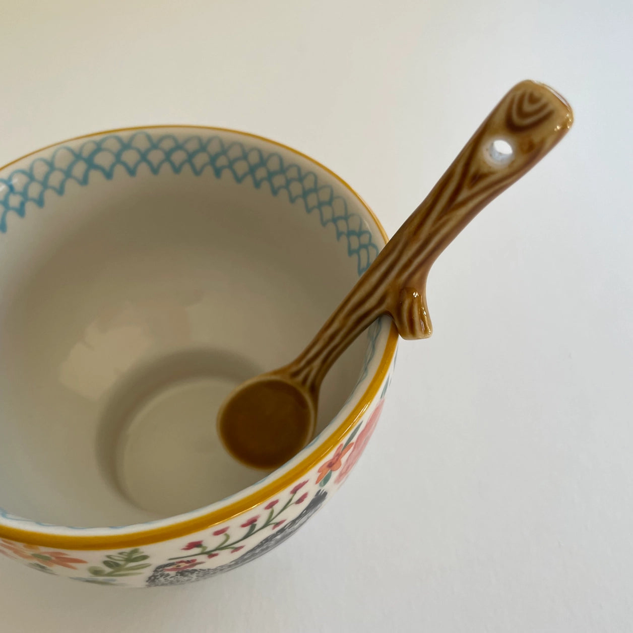 Ceramic bowl with floral patterns and a wooden spoon on a white background