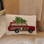 Decorative pillow with a truck and Christmas tree design on a beige couch.