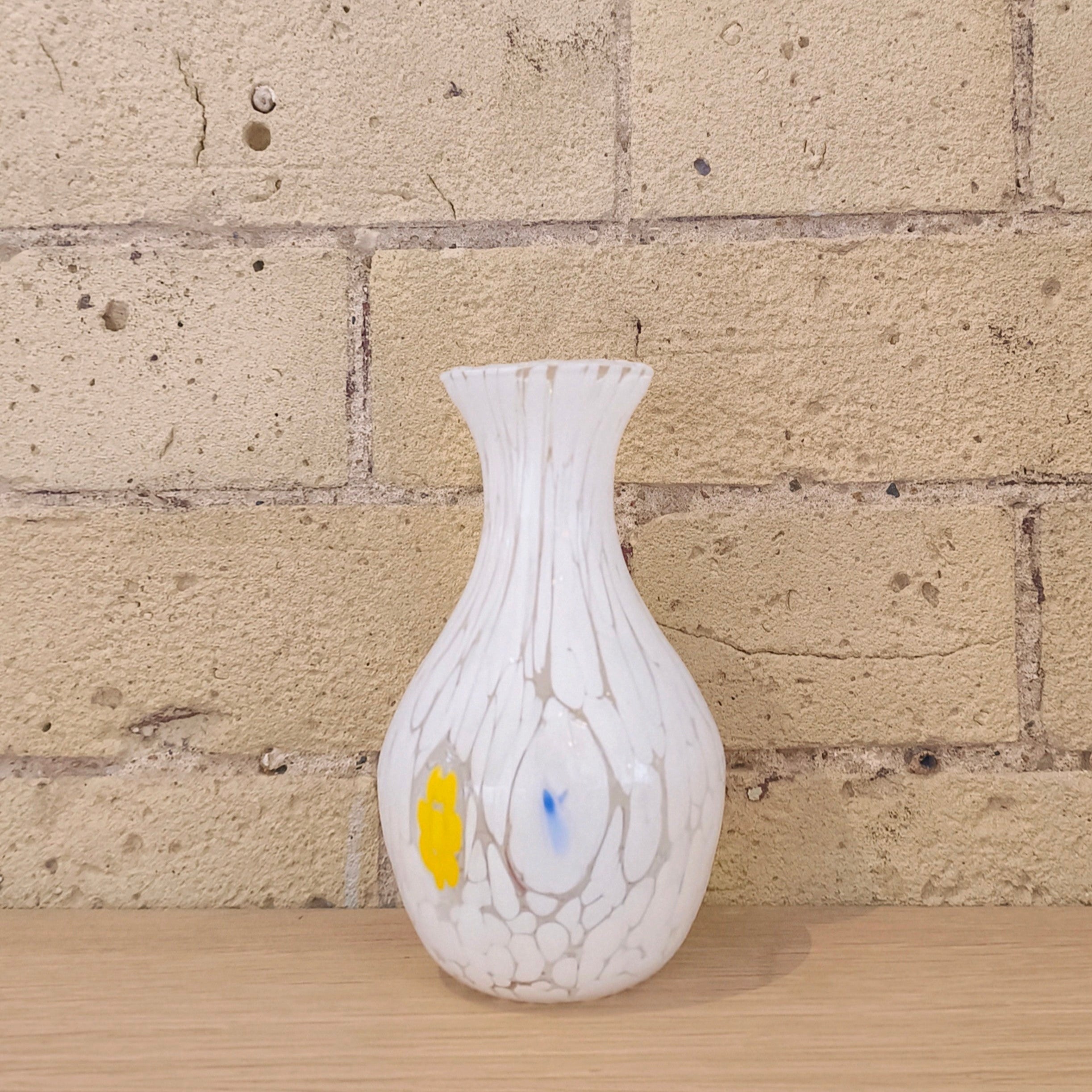 White textured vase with colorful accents on a wooden surface against a brick wall.